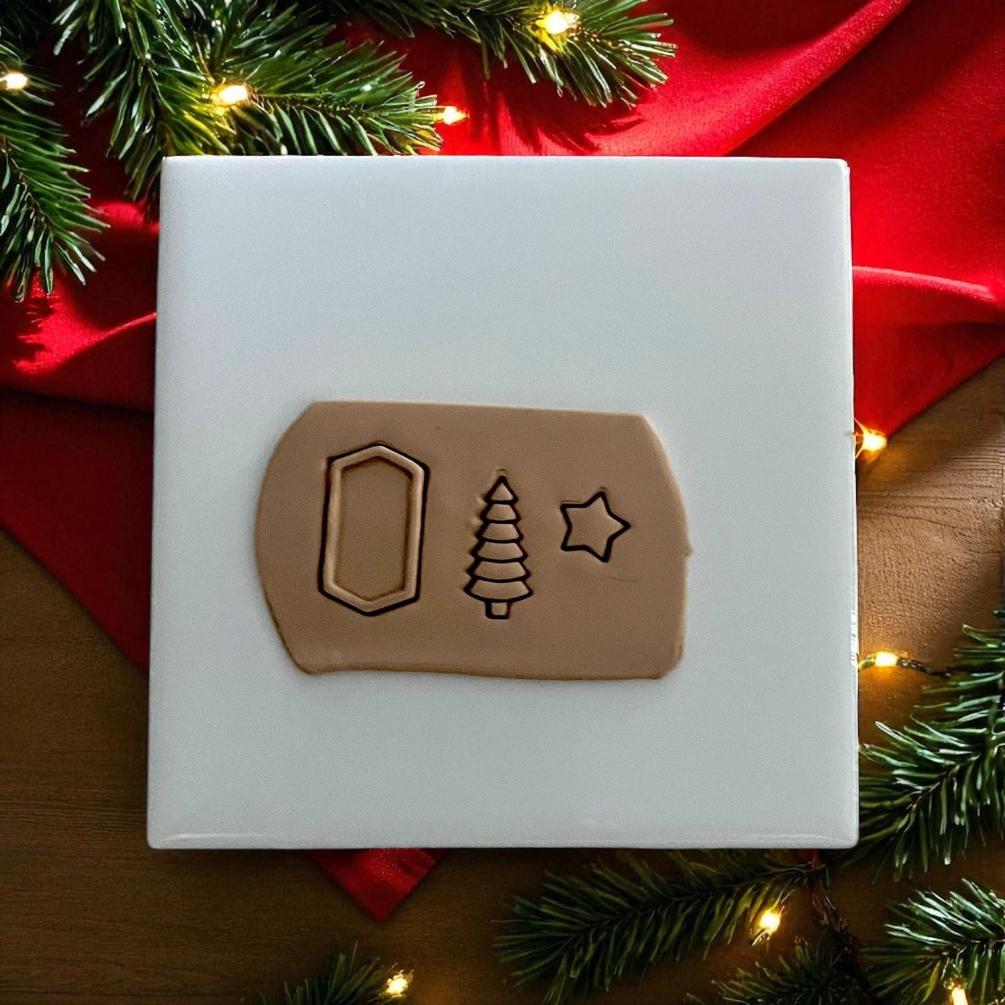 Polymer clay impressions of Christmas tree, frame, and star on tan clay sheet with holiday lights