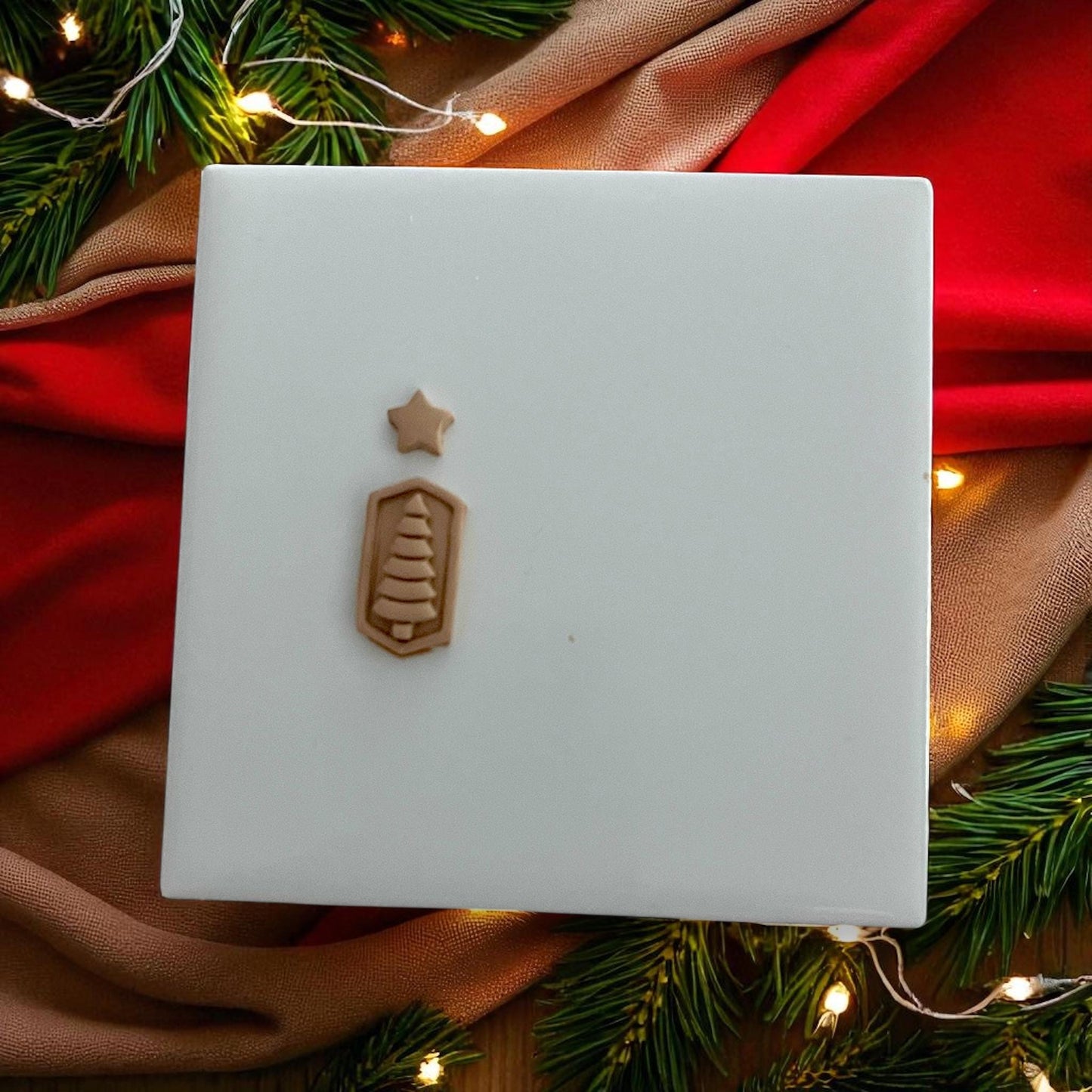 Small Christmas tree and star clay pieces on white tile with festive lights and greenery
