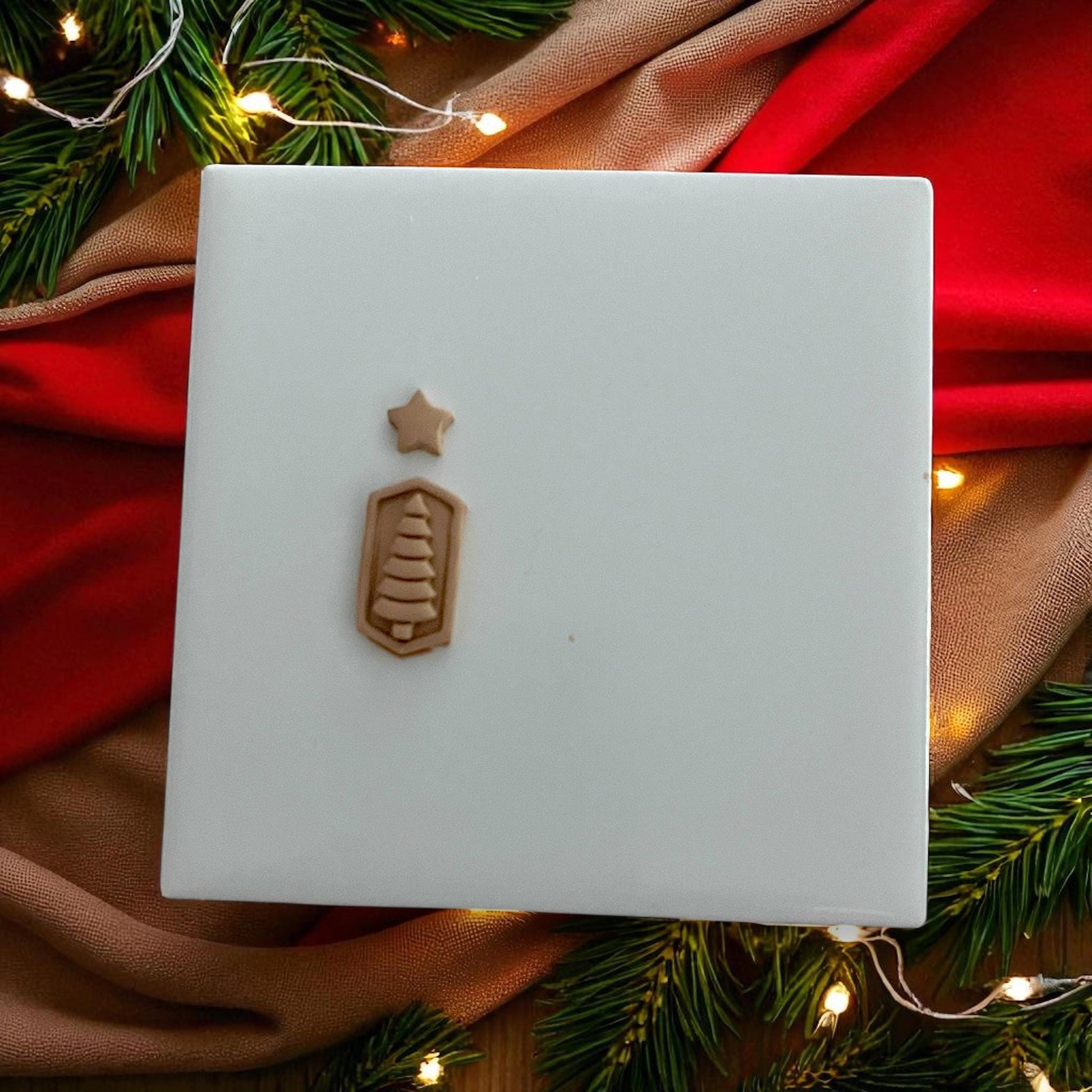 Small Christmas tree and star clay pieces on white tile with festive lights and greenery