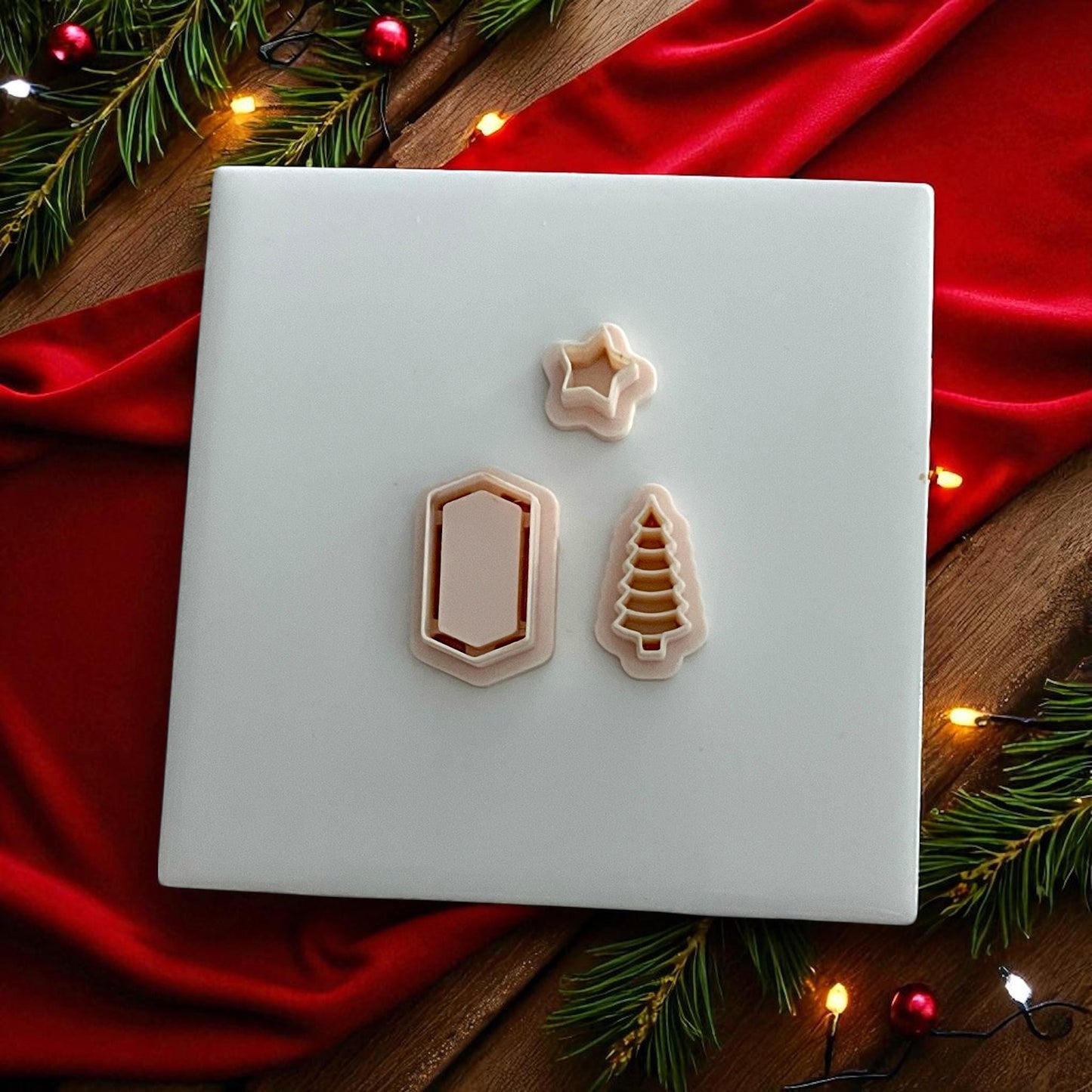 Set of white polymer clay cutters in shapes of tree, star, and frame on red festive cloth