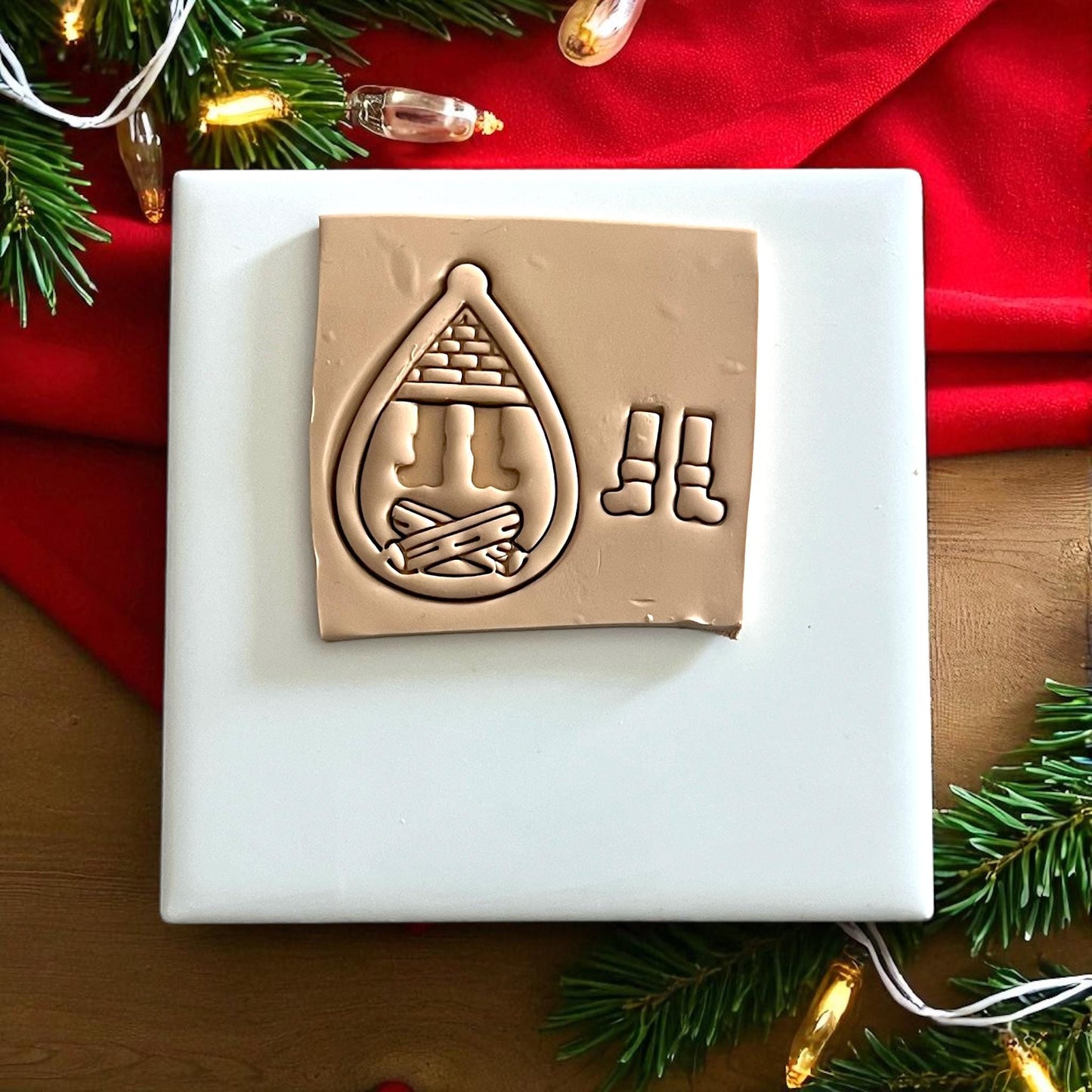 Santa boots polymer clay cutter and imprint on white tile with red cloth and Christmas greenery