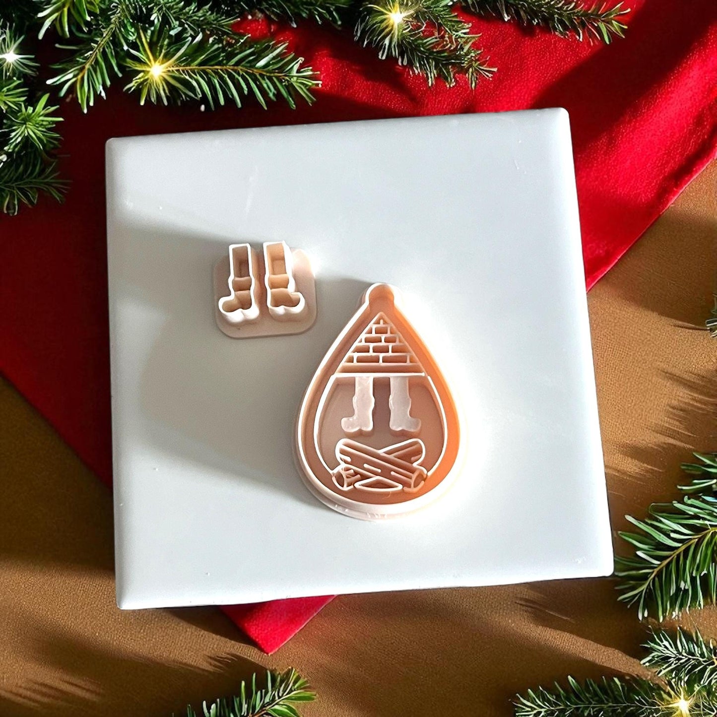 Christmas fireplace clay cutter surrounded by pine branches and festive red decor