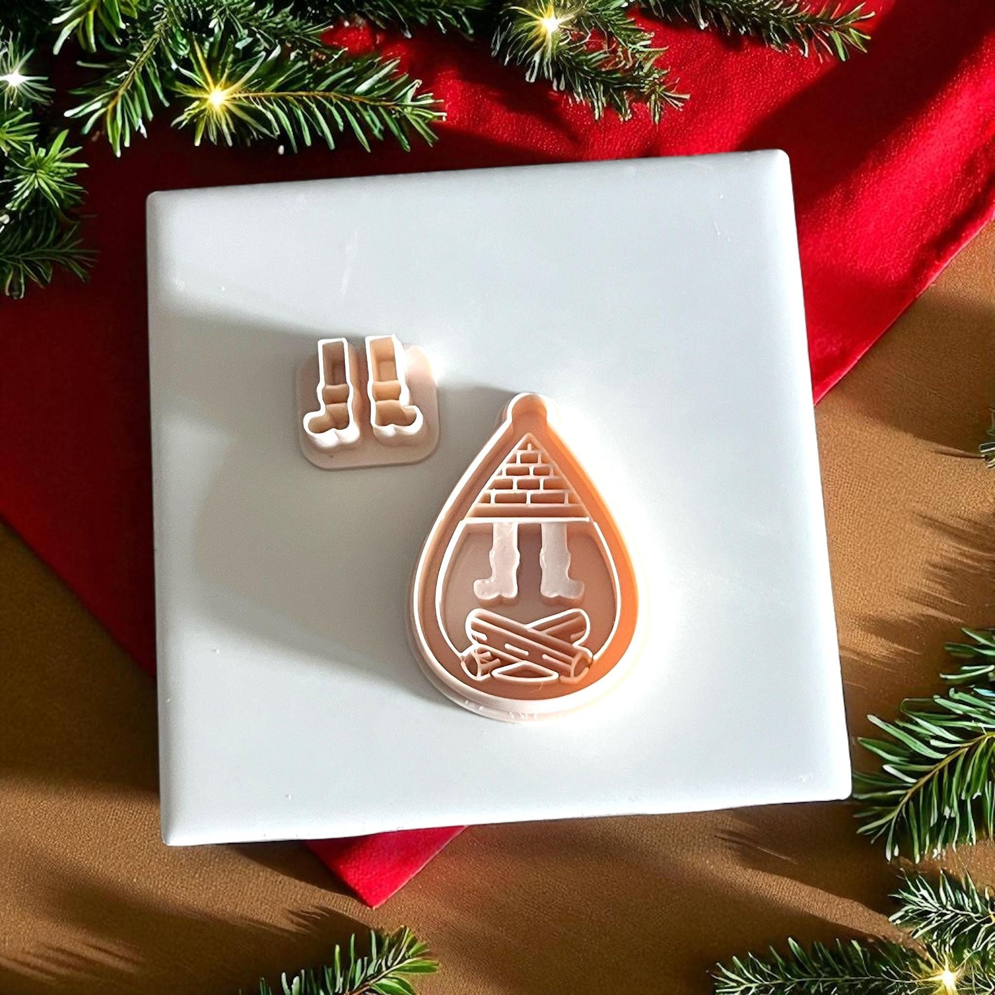 Christmas fireplace clay cutter surrounded by pine branches and festive red decor