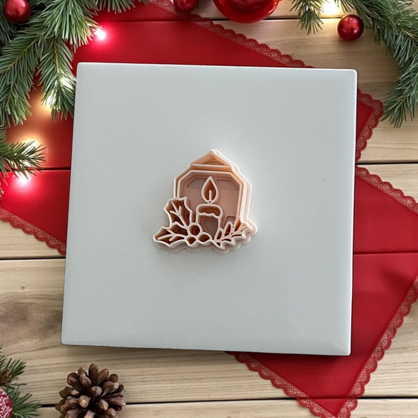 Holiday candle polymer clay cutter on white tile with pine branches and red ribbon
