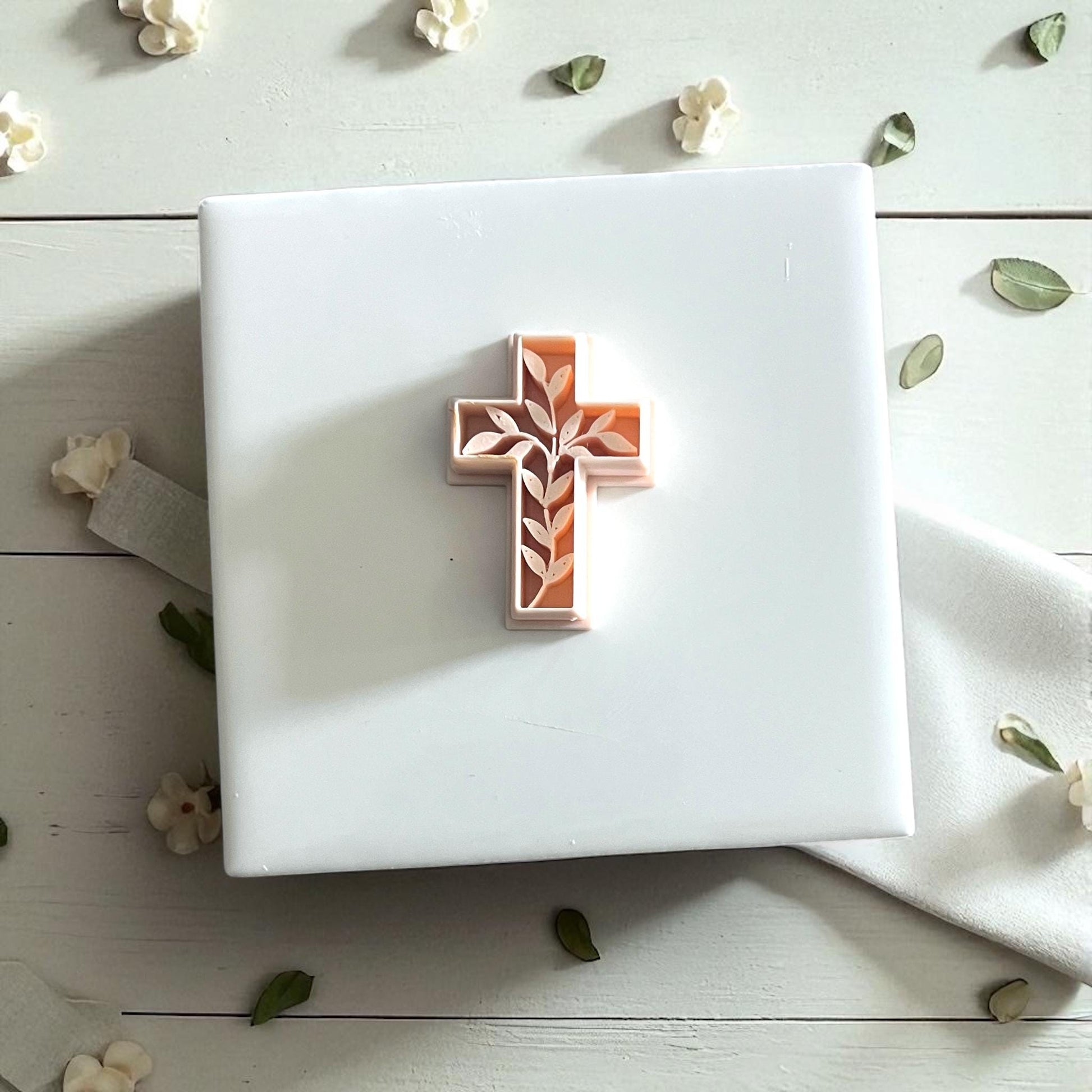 Small ivy cross cutter on white tile with petals and leaves