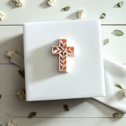 Small ivy cross cutter on white tile with petals and leaves