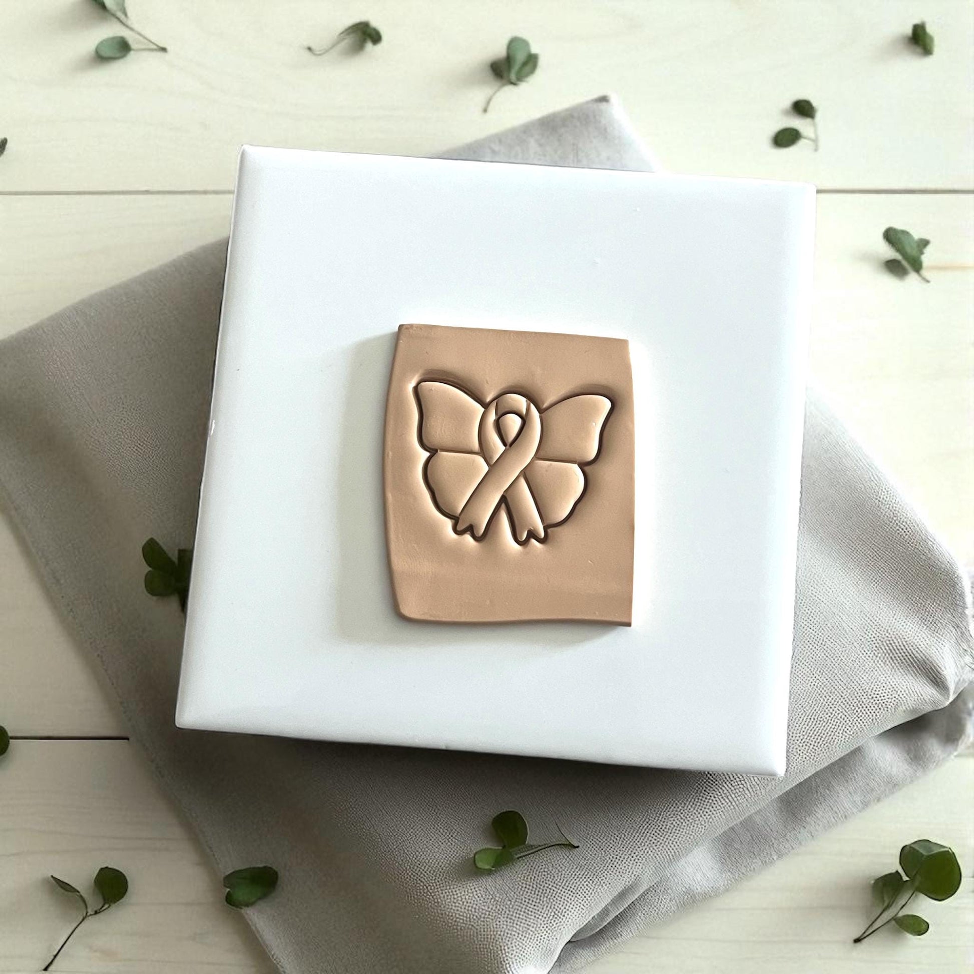 Butterfly ribbon polymer clay cutter on white tile with beige napkin and greenery