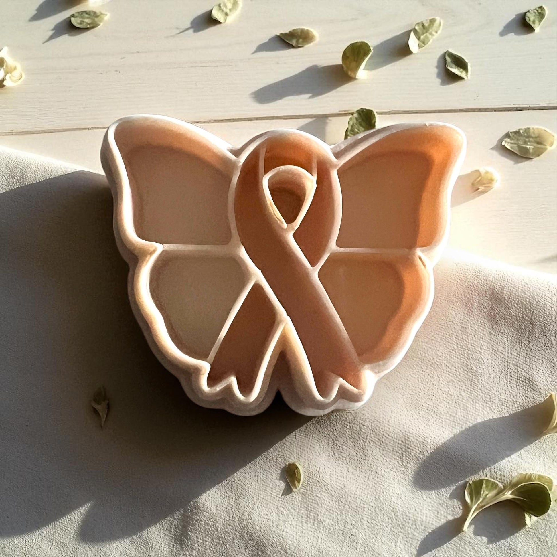 Close-up of butterfly ribbon clay impression surrounded by leaves