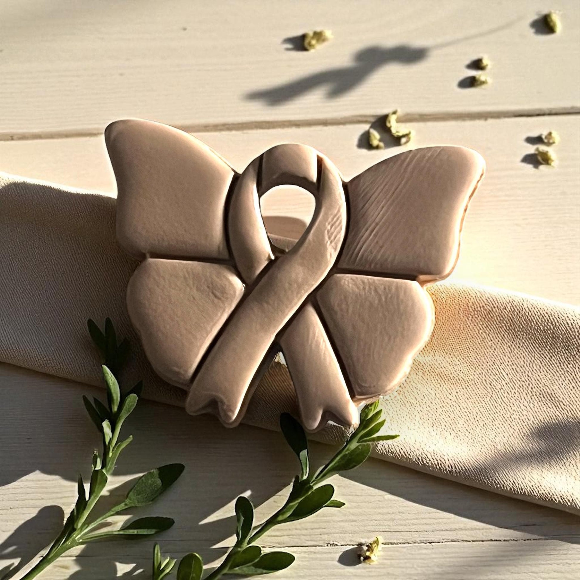 Butterfly ribbon cutter and clay impression on white tile surrounded by greenery