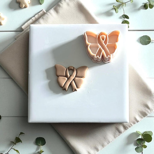 Awareness ribbon butterfly clay impression resting on fabric with green leaves