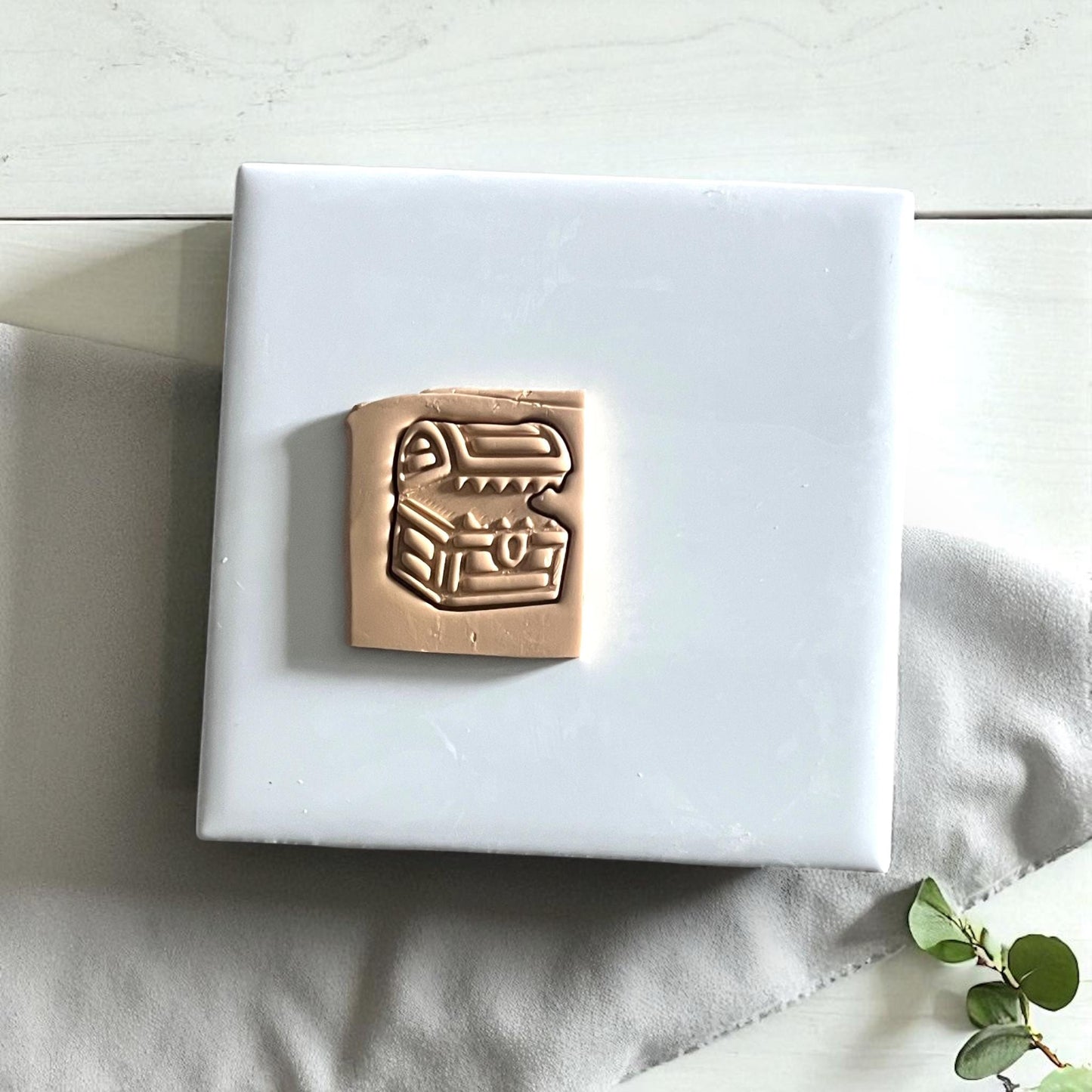Polymer clay mimic chest cutter on white fabric with green leaves
