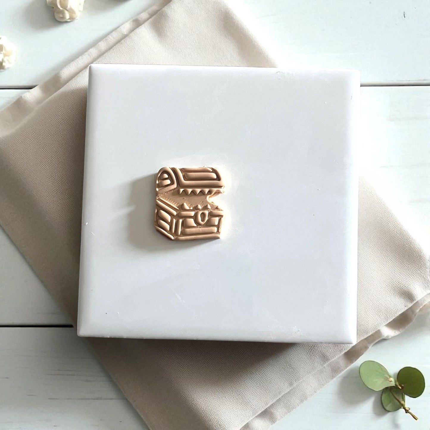 Small mimic chest clay cutter on white tile surrounded by leaves