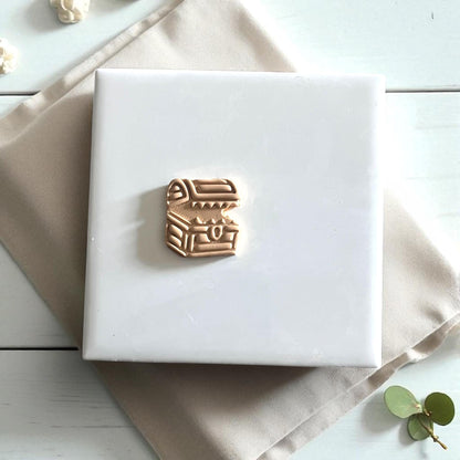 Small mimic chest clay cutter on white tile surrounded by leaves