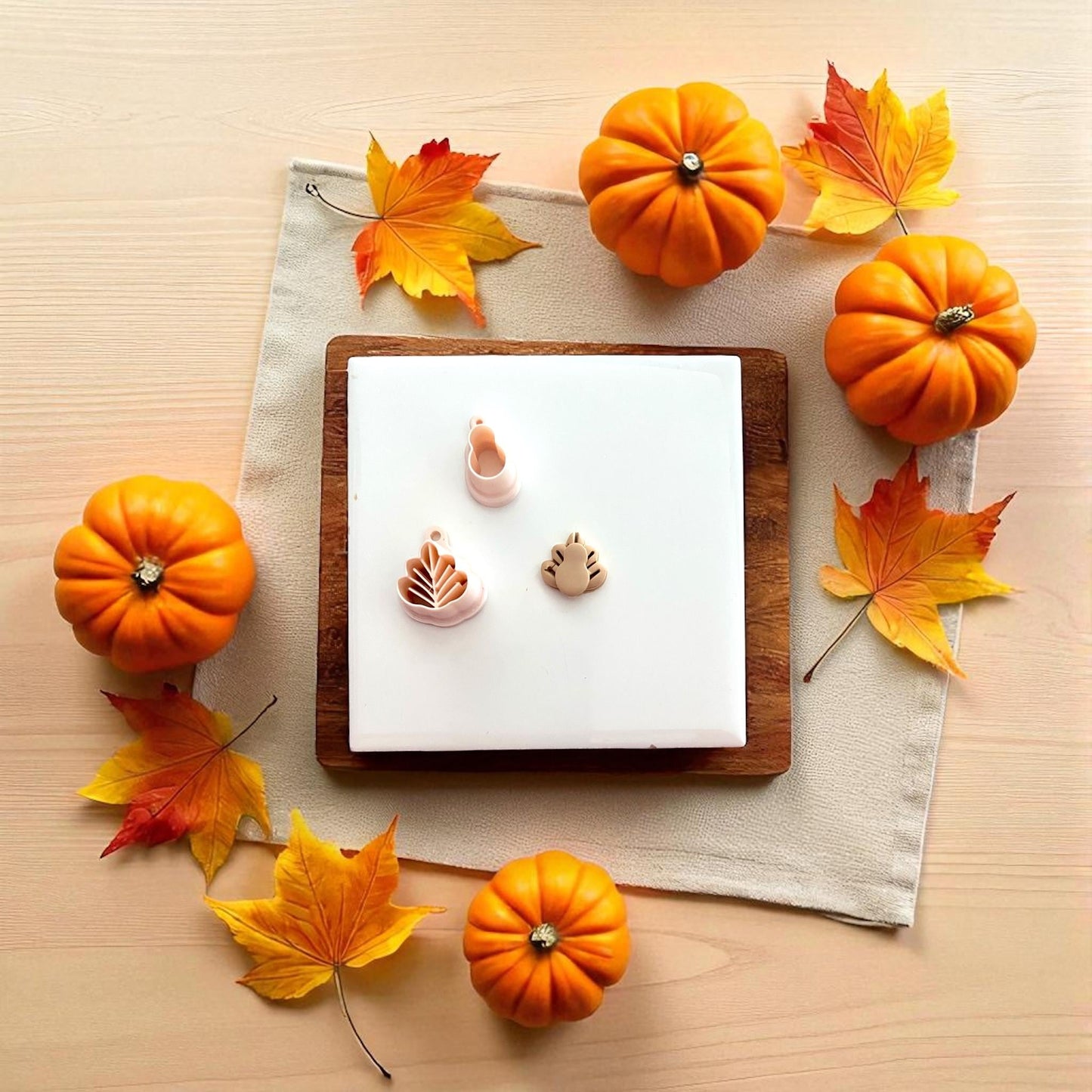 Pair of clay turkey designs on wooden plate surrounded by pumpkins and fall leaves