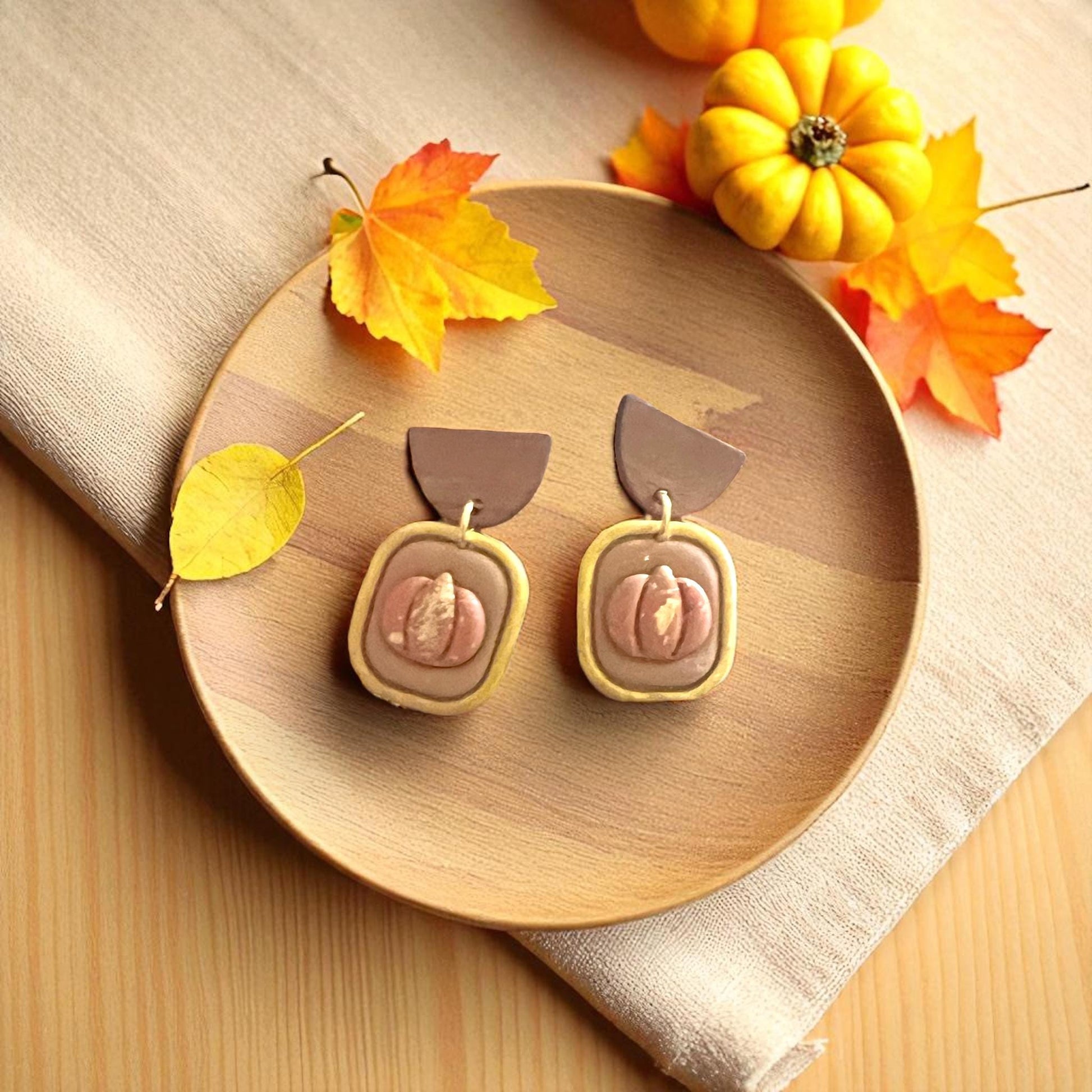 Autumn pumpkin clay earrings on wooden plate surrounded by pumpkins and leaves