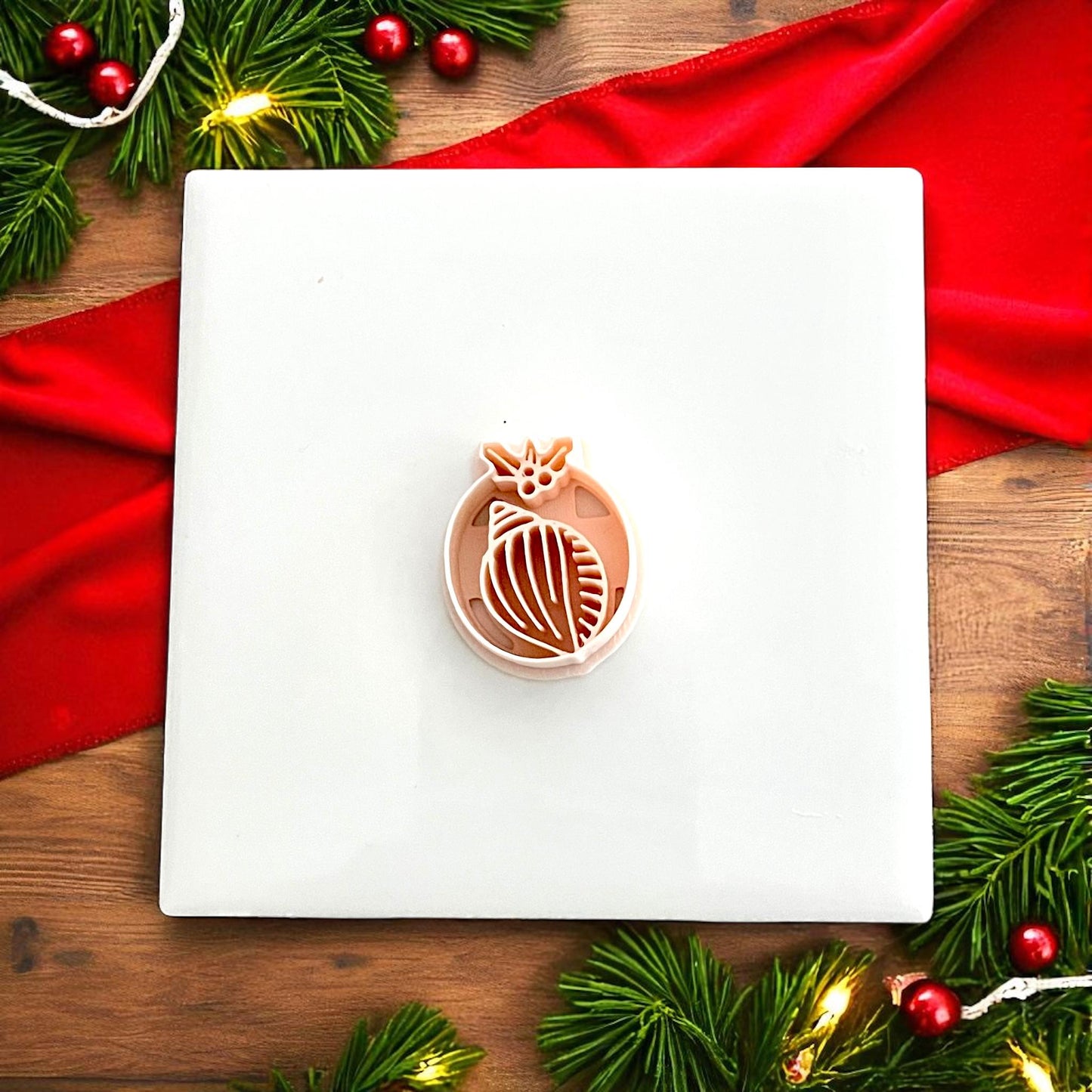 Shell clay cutter shown on white tile with Christmas greenery and red decorations