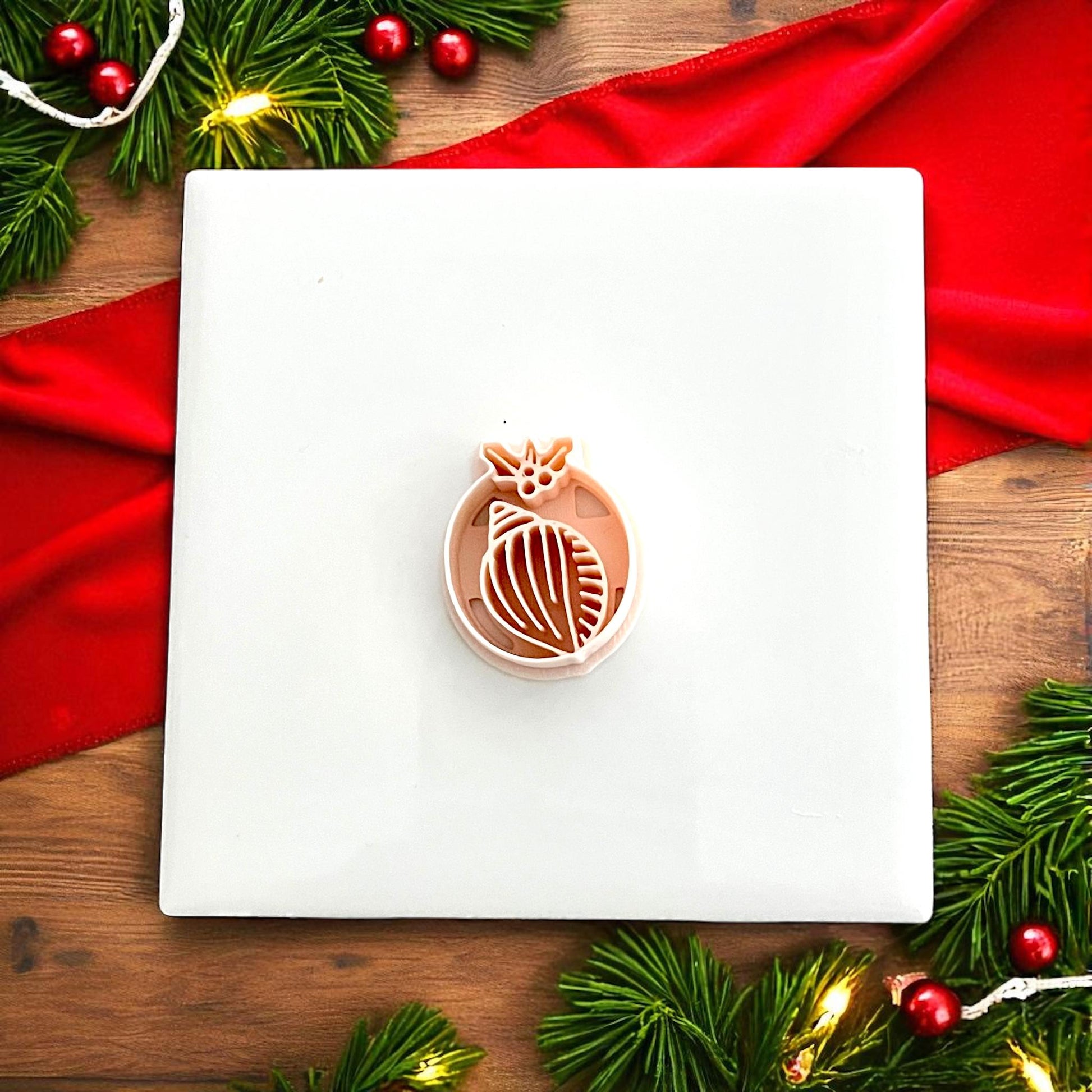 Shell clay cutter shown on white tile with Christmas greenery and red decorations