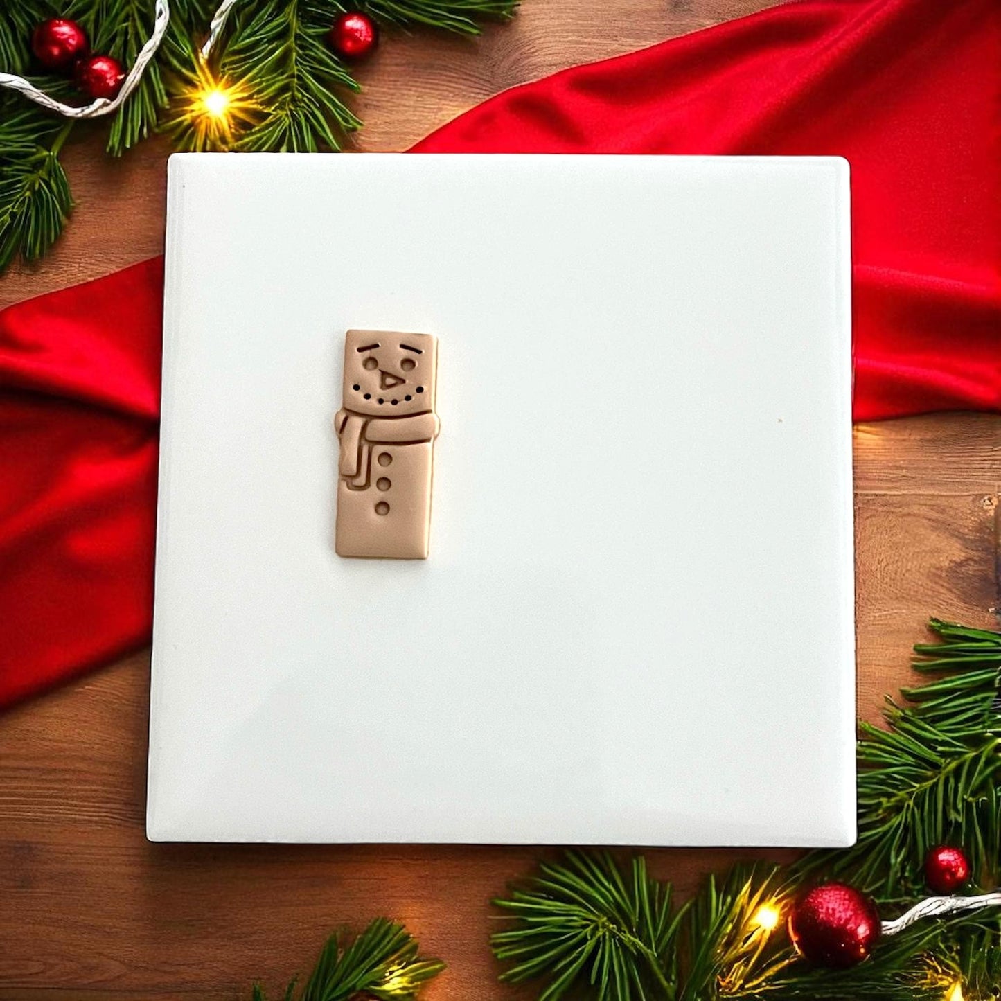 Large snowman bar clay design on plate surrounded by Christmas lights and greenery