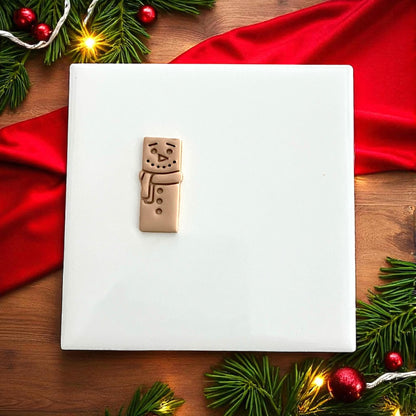 Large snowman bar clay design on plate surrounded by Christmas lights and greenery