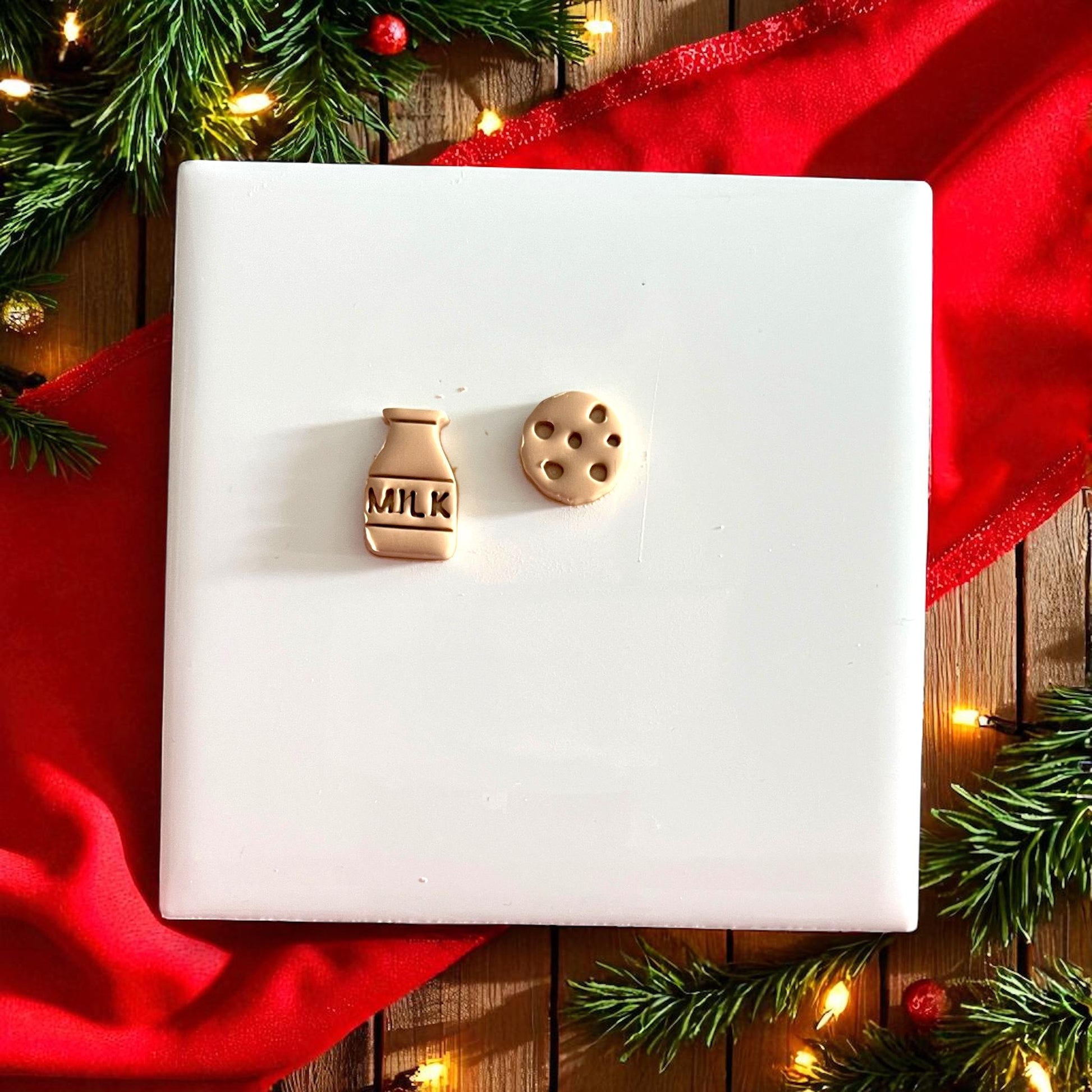 Christmas milk and cookie clay impression on tile surrounded by red fabric and greenery