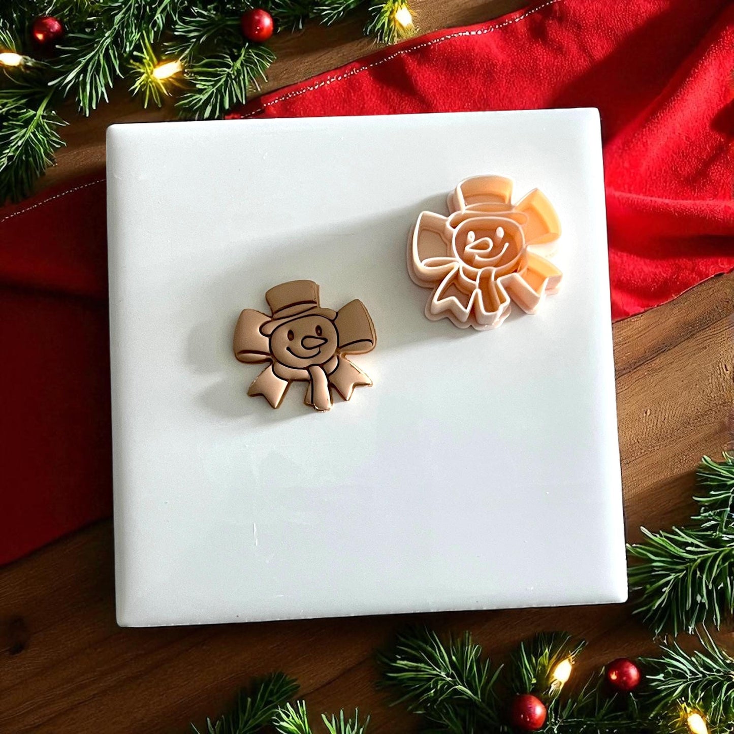 Clay cutter and impression of snowman bow shown on white tile with festive red fabric