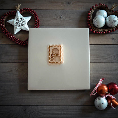 Small snowman postage clay imprint centered on white tile with holiday decor