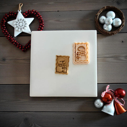 Two snowman postage clay imprints side by side with ornaments and star decoration