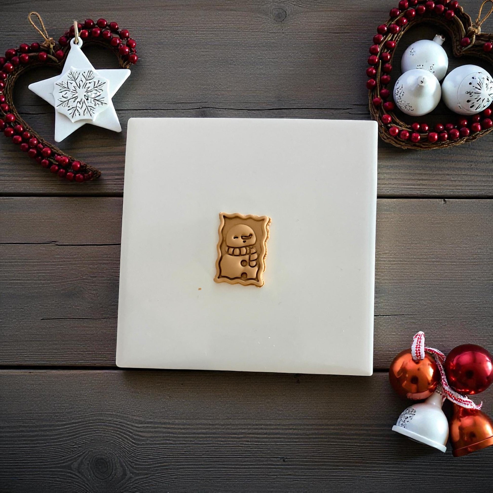 Tan snowman postage stamp clay imprint on wood background with Christmas ornaments