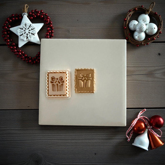Two gift stamp clay imprints side by side on white tile with Christmas decor