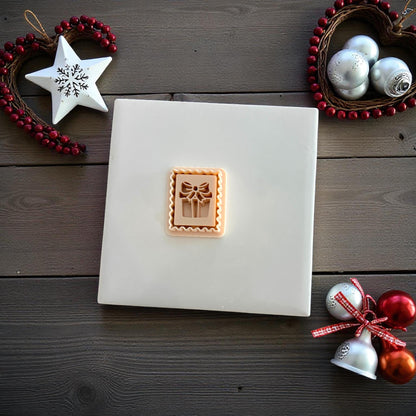 Small gift stamp clay imprint centered on white tile with festive holiday decor