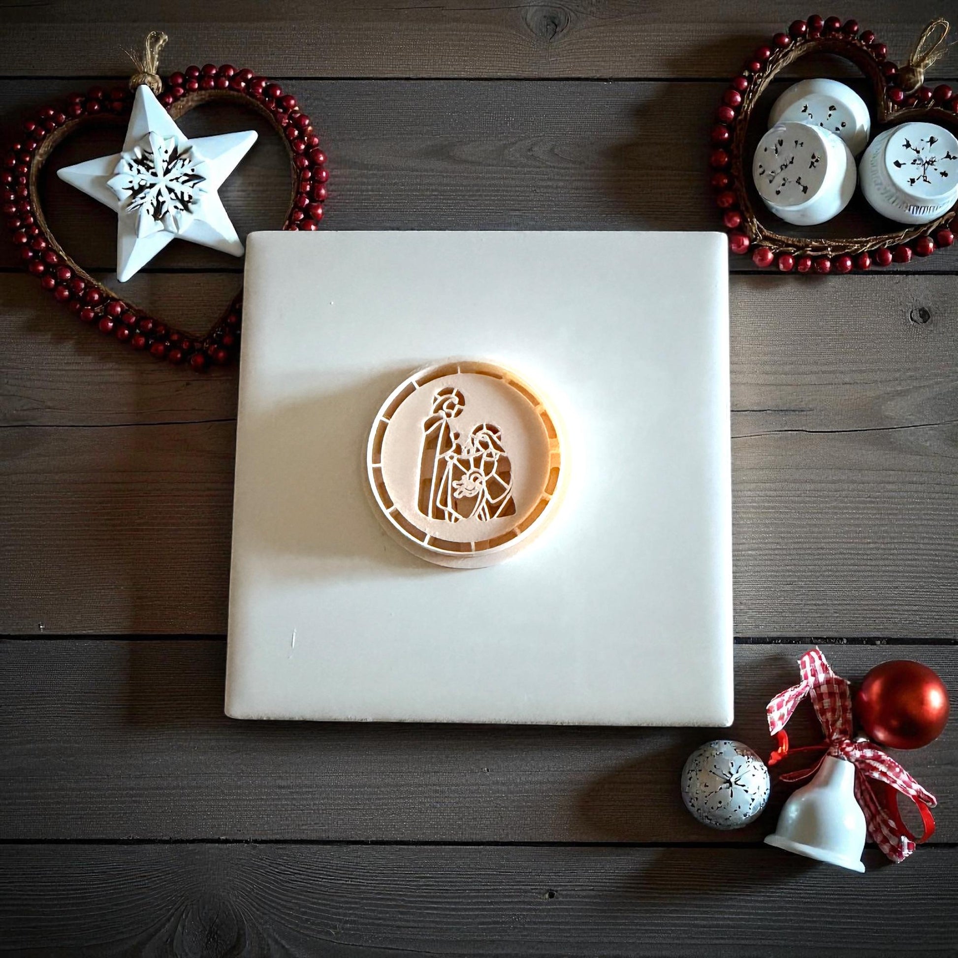 Nativity clay imprint centered on white tile with holiday ornaments and red ribbon