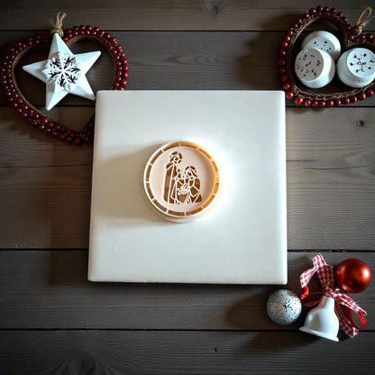 Nativity clay imprint centered on white tile with holiday ornaments and red ribbon