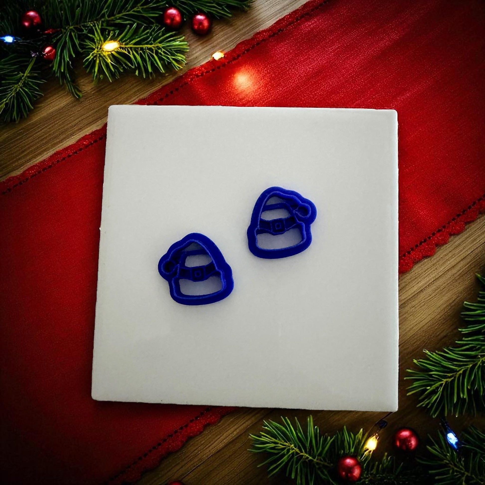 Blue Santa hat polymer clay cutters on wooden plate with red fabric and pine branches