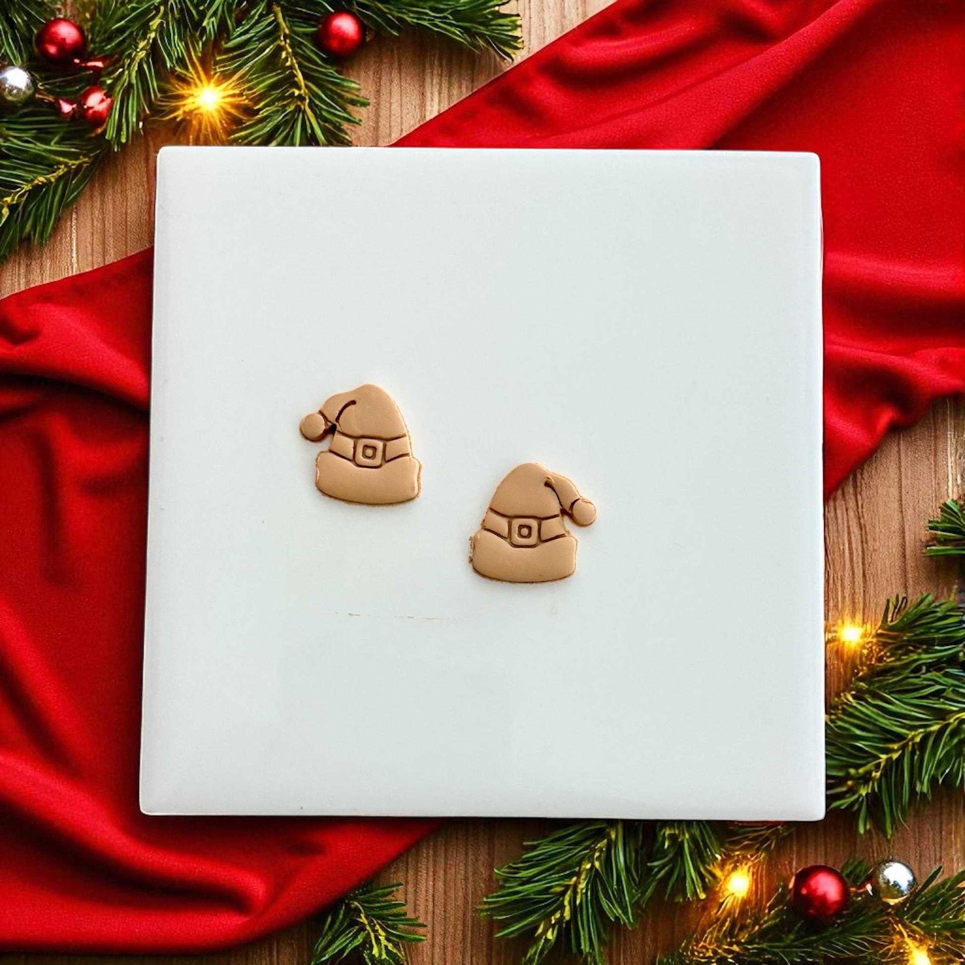 Santa hat clay imprints on white tile with red fabric and pine branches