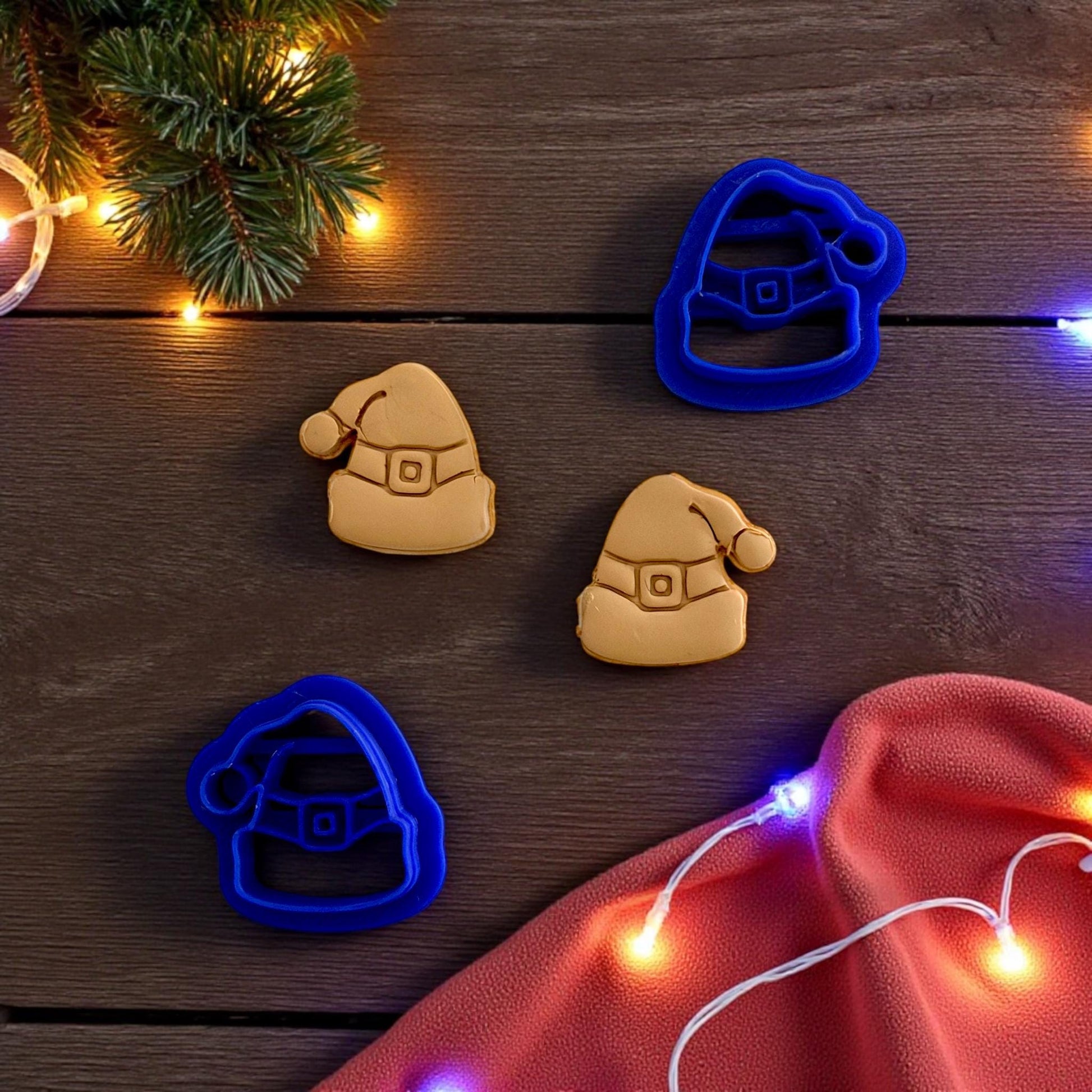 Close up of Blue Santa hat clay cutters with tan clay imprints on wooden surface and string lights