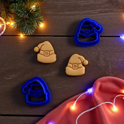 Close up of Blue Santa hat clay cutters with tan clay imprints on wooden surface and string lights