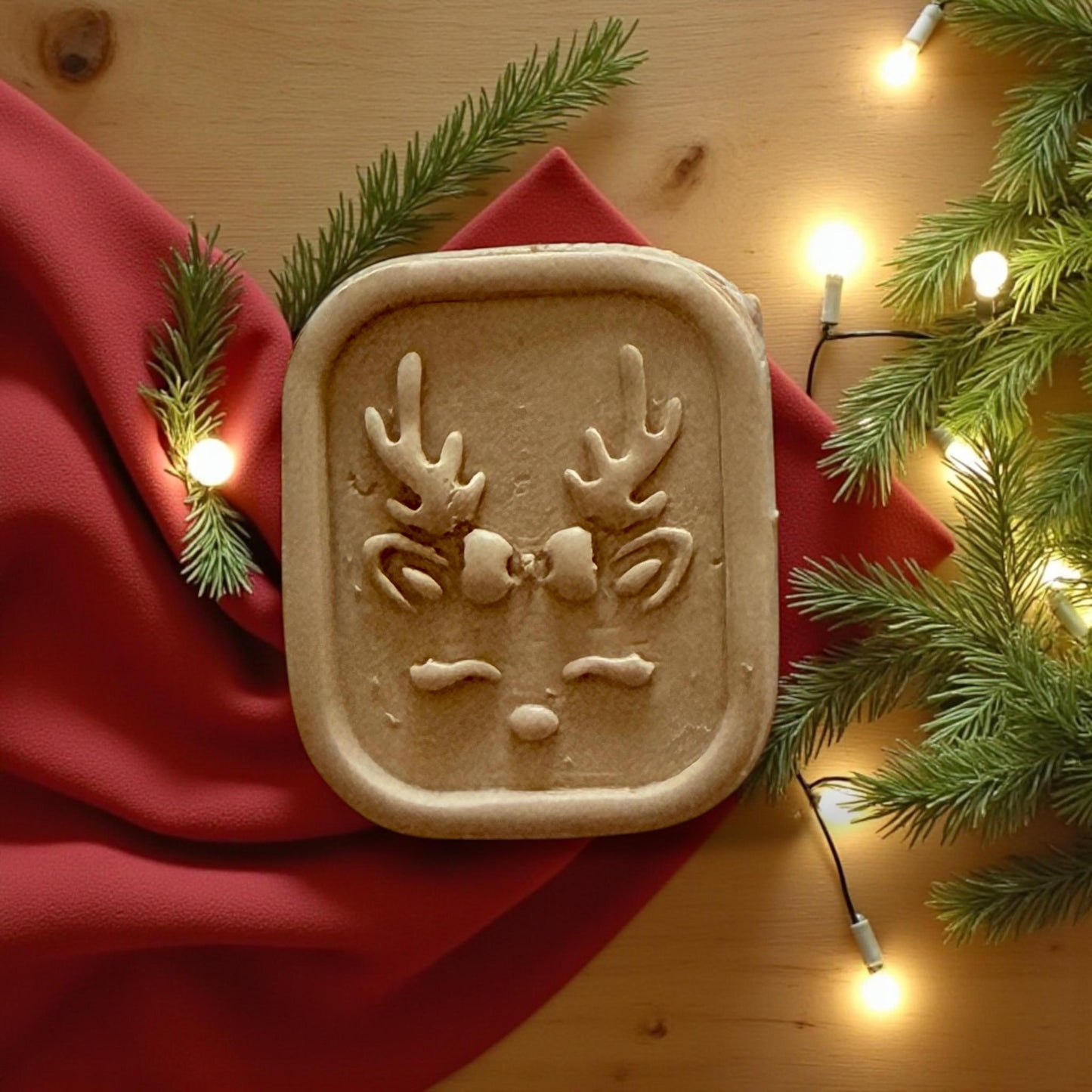 Reindeer clay imprint on red fabric with glowing lights and pine greenery