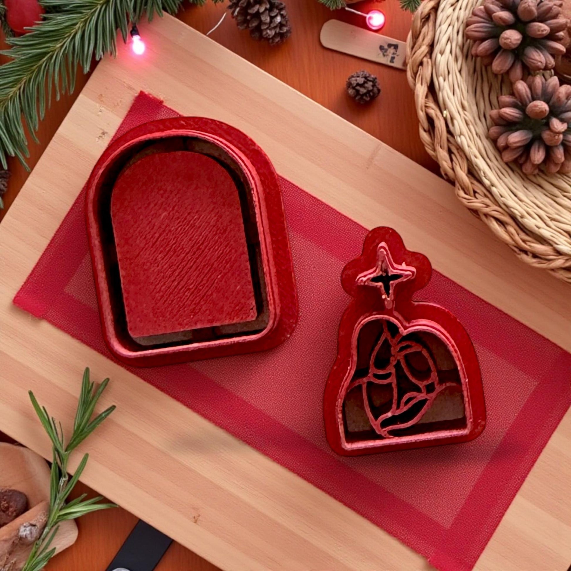 Red Nativity clay cutters on wooden board with holiday greenery and woven basket