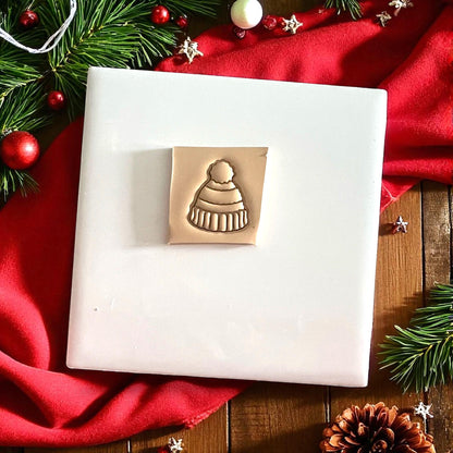 Polymer clay beanie cutter displayed on white tile with holiday background