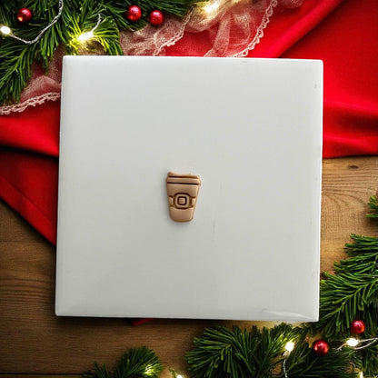 Small Santa coffee cup clay impression on white tile surrounded by festive décor