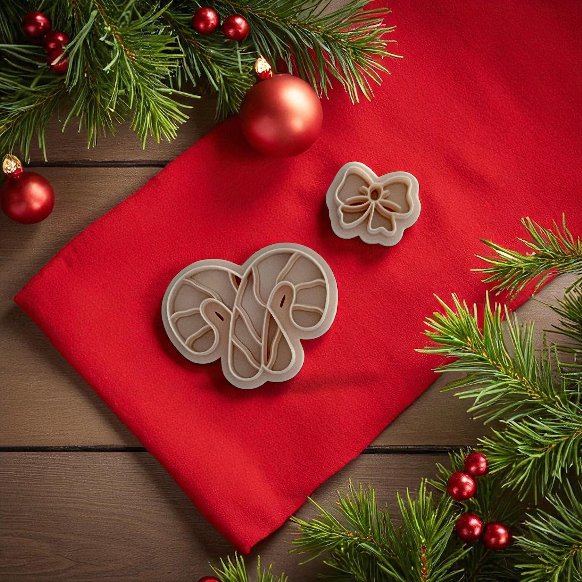 Candy cane bow polymer clay cutters displayed on red fabric with pine branches and ornaments