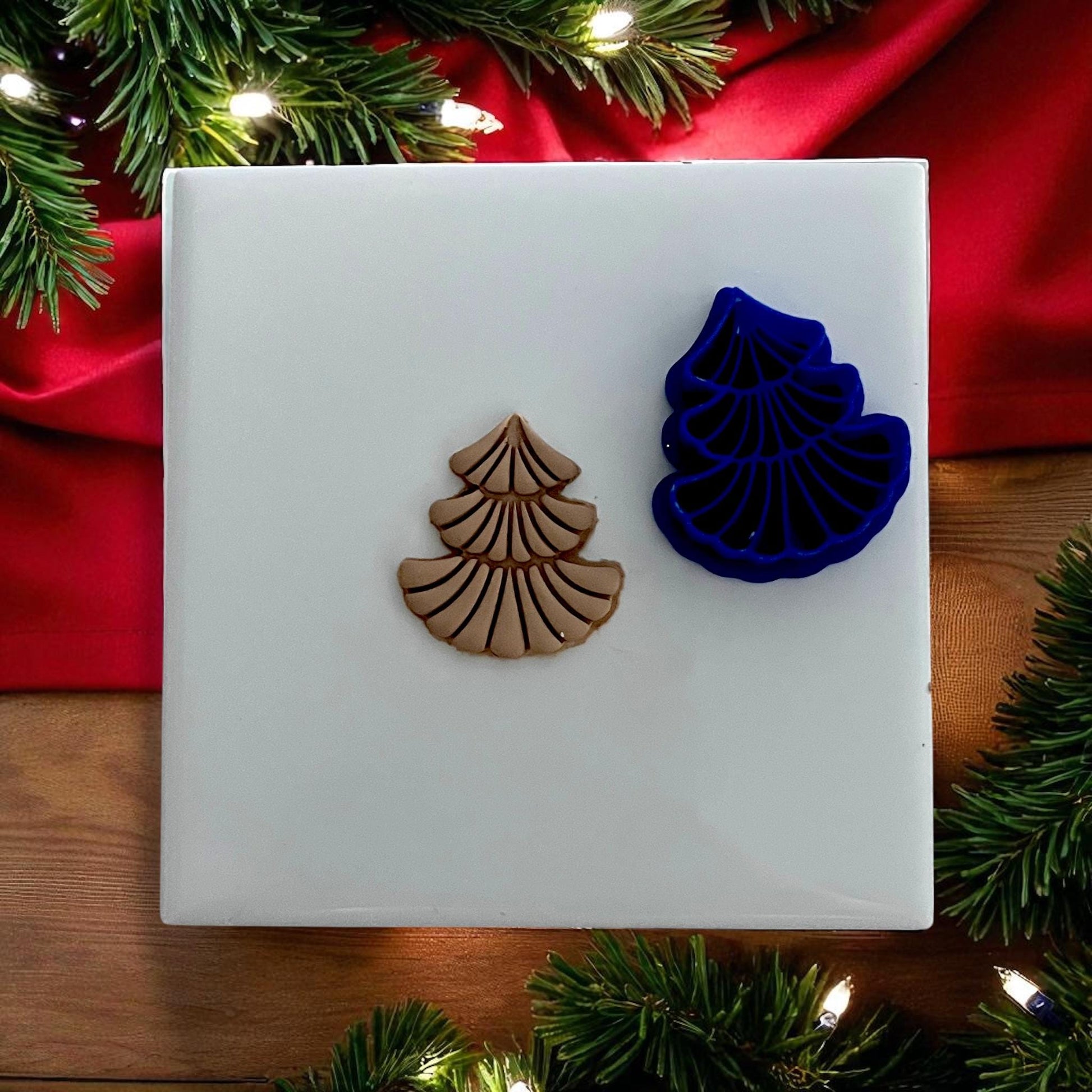Scalloped Christmas tree polymer clay cutter and impression on white tile with red holiday fabric