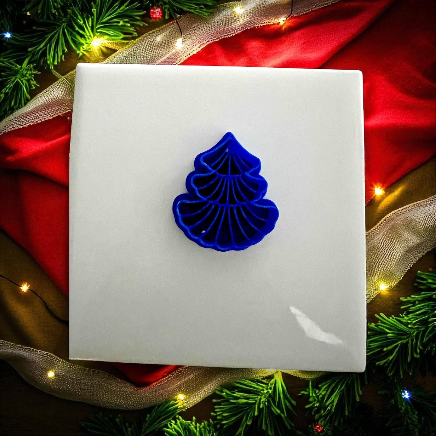Blue scalloped tree clay cutter on white tile with red holiday background