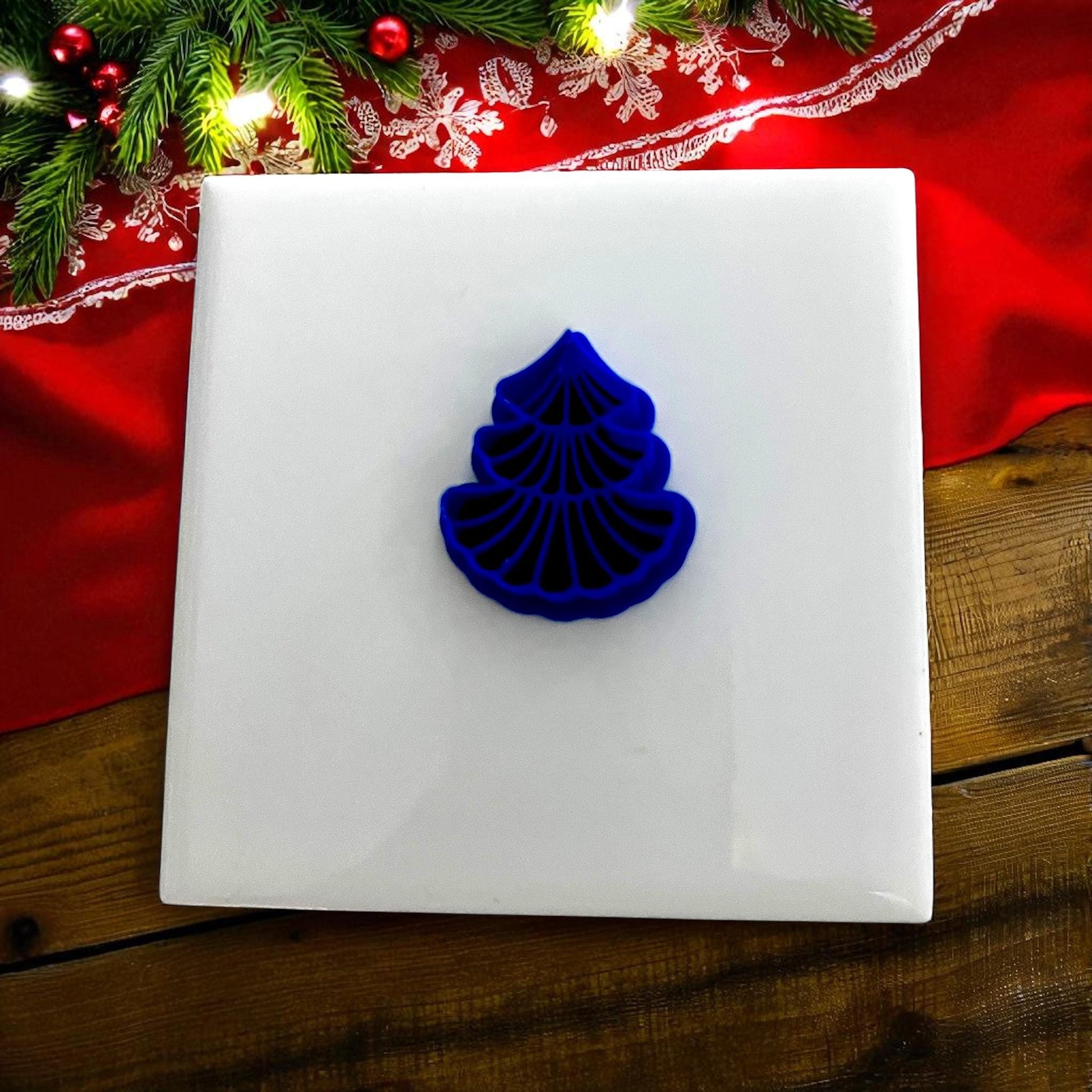 Blue scalloped tree clay cutter on white tile with red holiday background