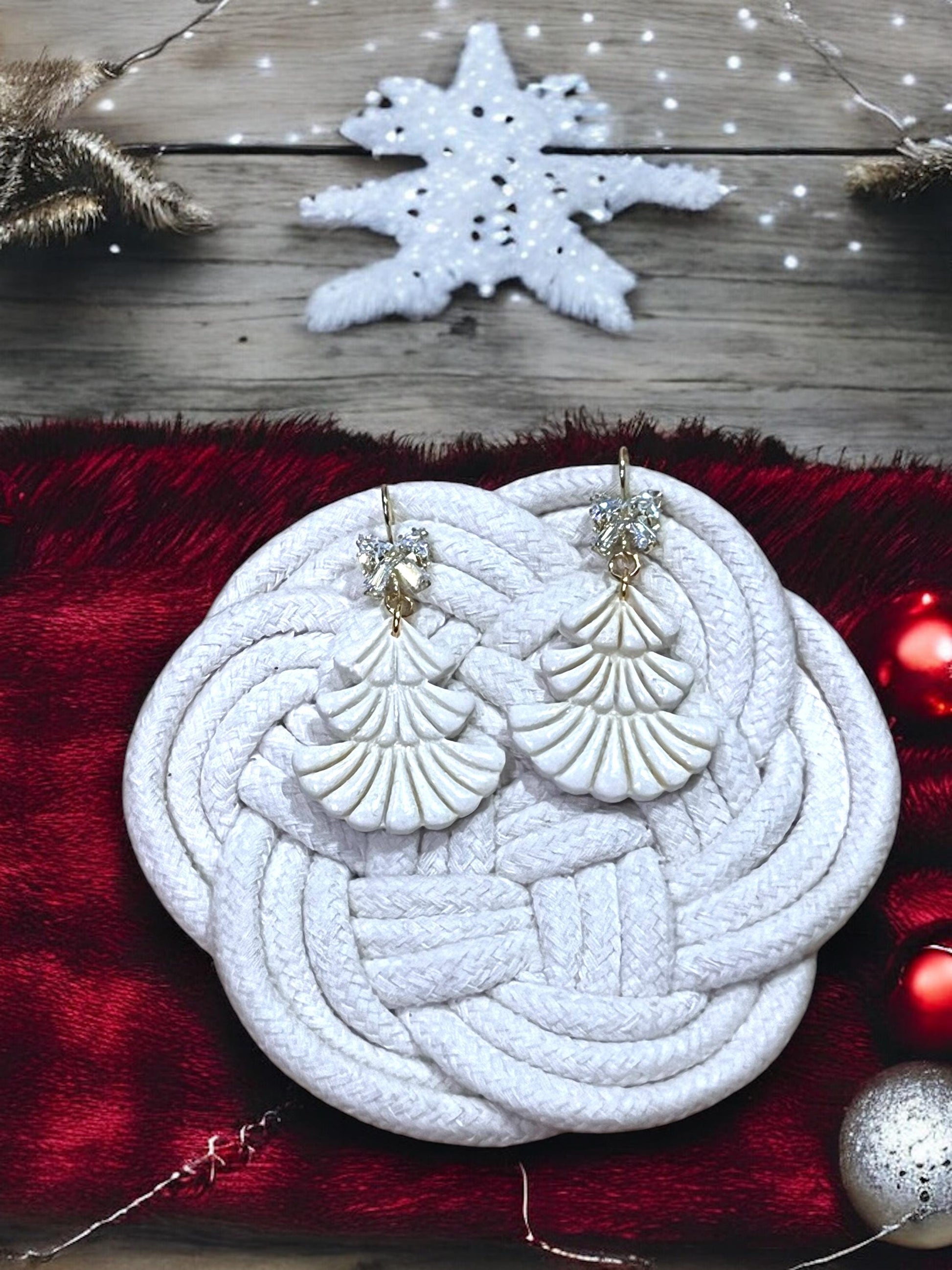White scalloped Christmas tree earrings with rhinestone tops displayed on woven white pad with snowflake backdrop