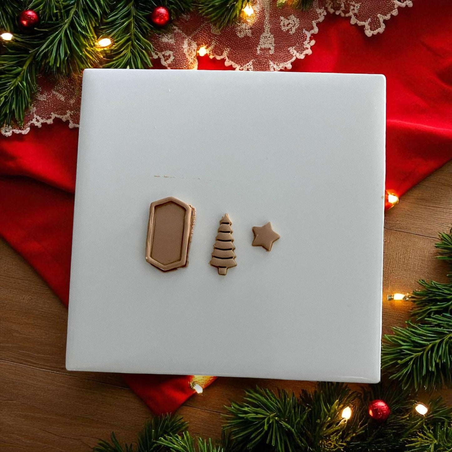 Tree, frame, and star polymer clay cutouts arranged on white tile with holiday background