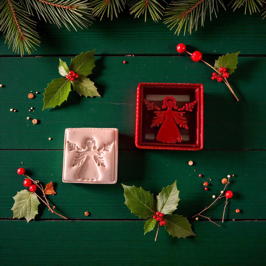 Angel clay imprint and red cutter surrounded by holly leaves and berries