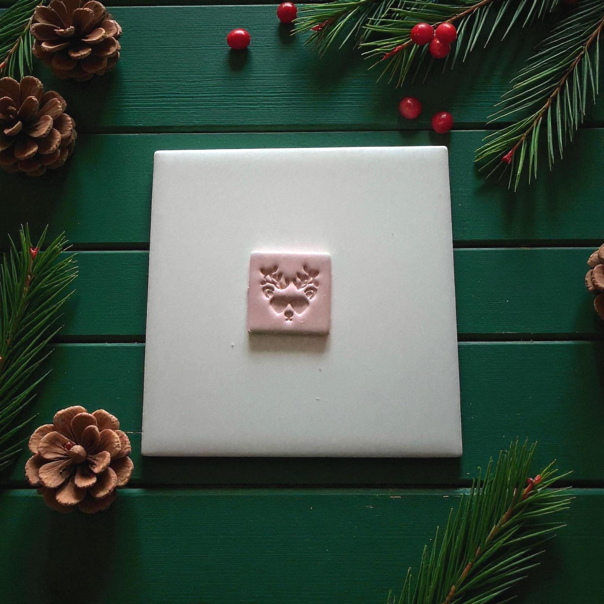 Square pink reindeer imprint centered on white tile with Christmas greenery