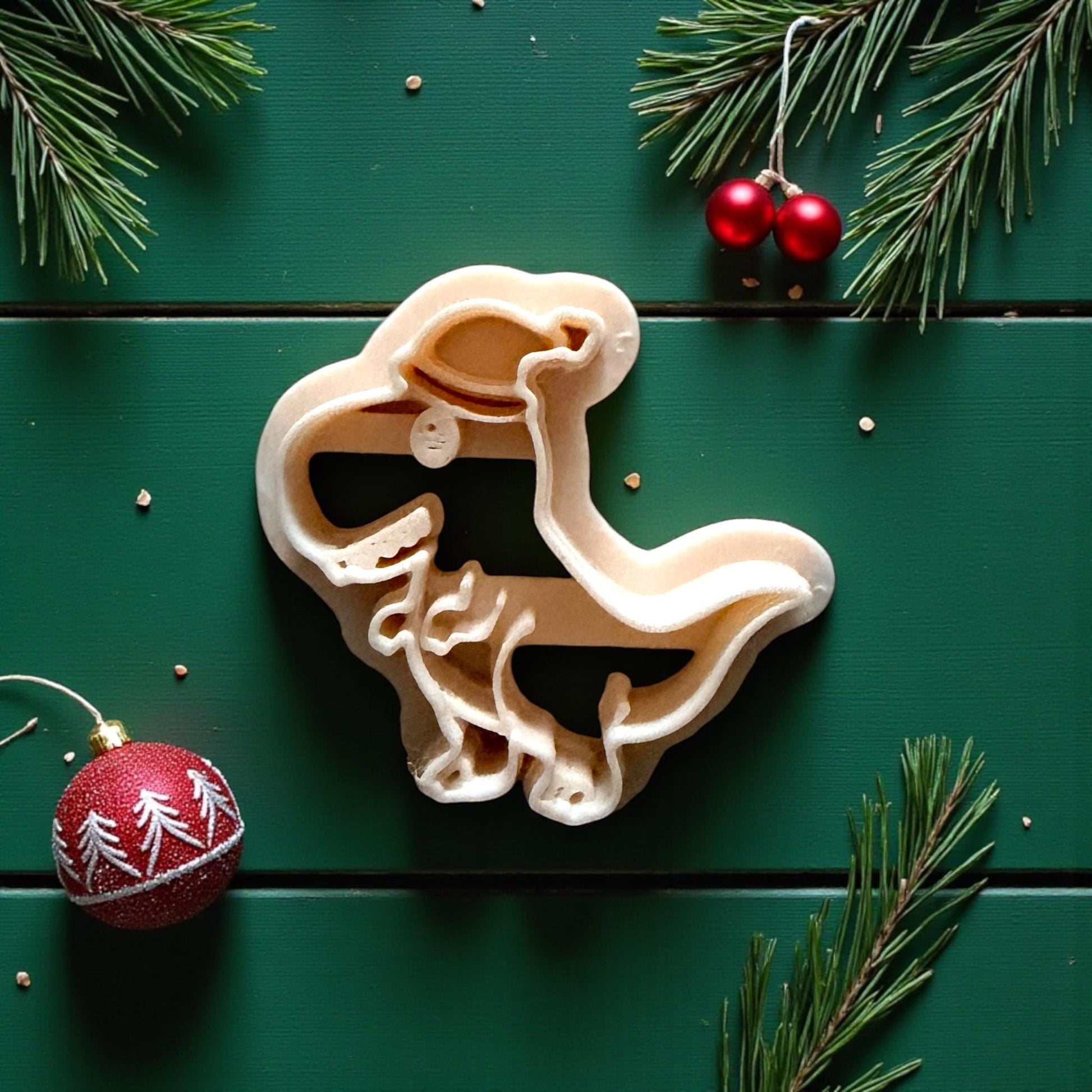 Close-up of cream dino cutter with Santa hat surrounded by pine branches and ornaments