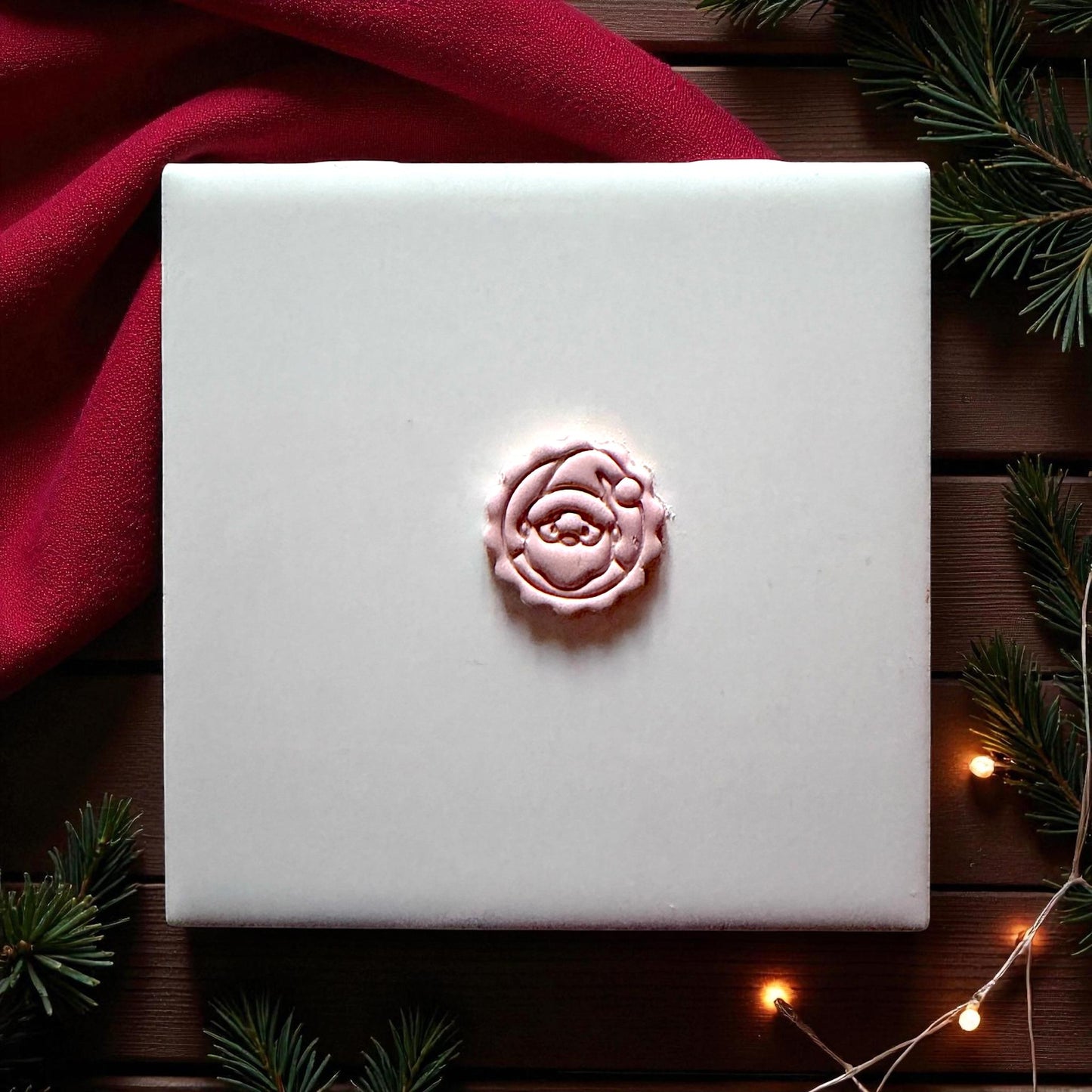 Centered pink Santa imprint on wood background with greenery and red fabric